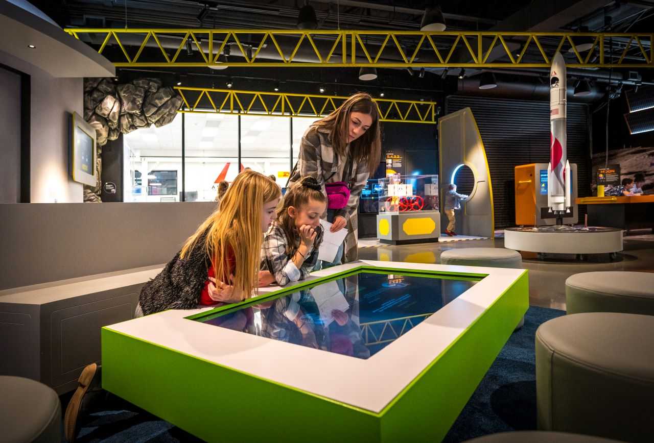 An instructor and two children gather around their digital ballots table at Moonshot Museum.